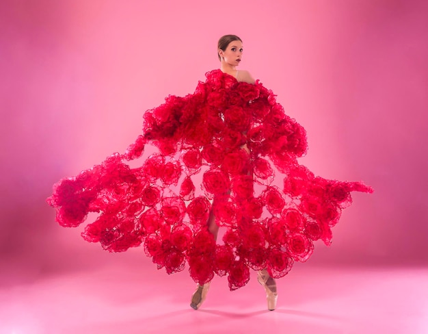 jovem bailarina em um estúdio de fotos em um vestido de capa feito de flores de rosa mostra movimentos de ballet