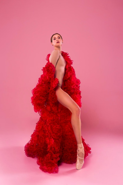jovem bailarina em um estúdio de fotos em um vestido de capa feito de flores de rosa mostra movimentos de ballet