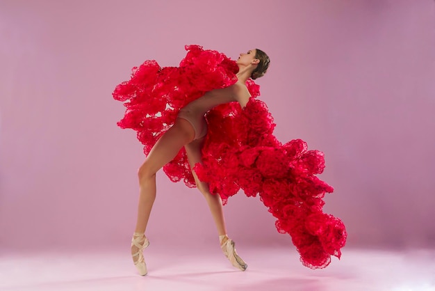 jovem bailarina em um estúdio de fotos em um vestido de capa feito de flores de rosa mostra movimentos de ballet