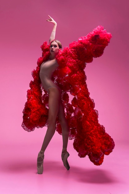 jovem bailarina em um estúdio de fotos em um vestido de capa feito de flores de rosa mostra movimentos de ballet