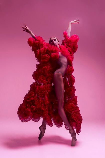 jovem bailarina em um estúdio de fotos em um vestido de capa feito de flores de rosa mostra movimentos de ballet