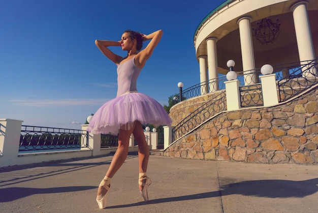 jovem bailarina em um tutu e sapatos de ponta com pés bonitos dança em um dia de verão em um pavilhão no terraço