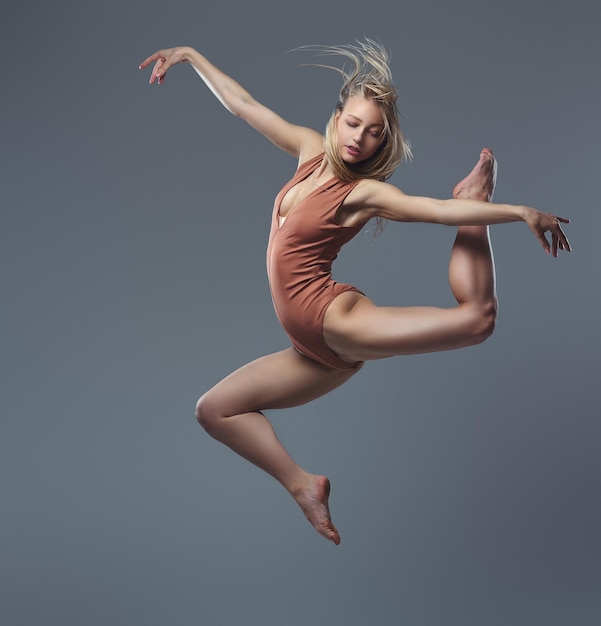 Jovem bailarina loira graciosa dança e pula em um estúdio. Isolado em um fundo cinza.