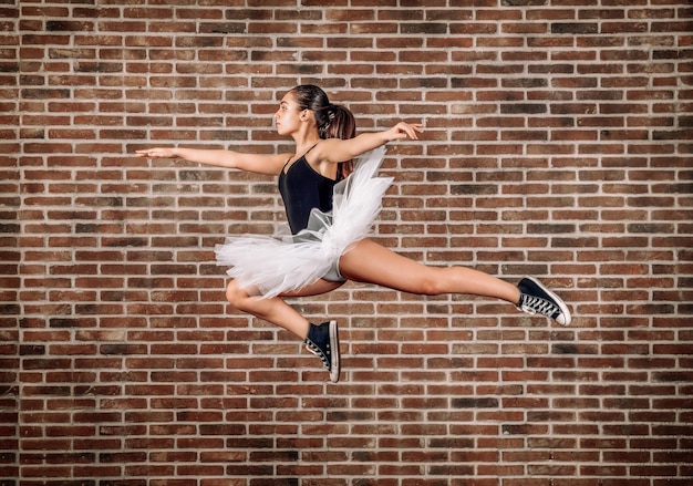 Jovem bailarina pulando contra a parede de tijolos