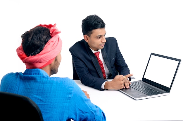 Jovem banqueiro indiano dando algumas informações ao agricultor no laptop no escritório.