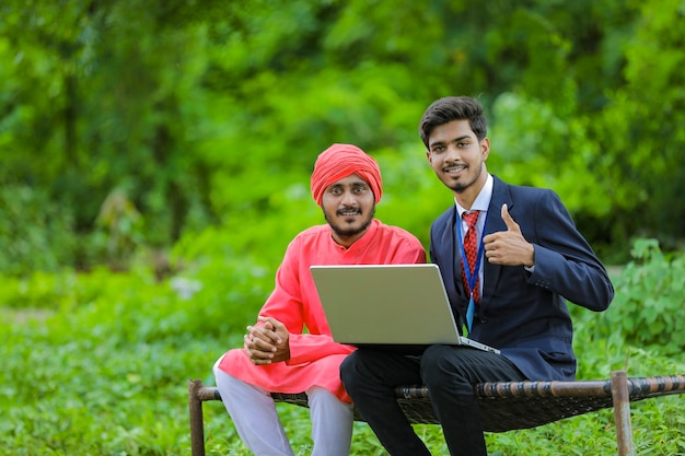 Jovem banqueiro indiano mostrando algumas informações ao fazendeiro no laptop no campo