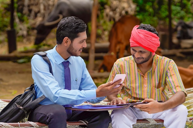 Jovem banqueiro indiano ou agrônomo mostrando alguns detalhes ao fazendeiro no smartphone.