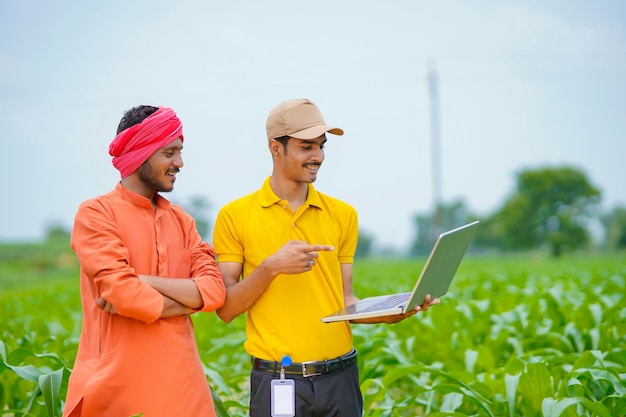 Jovem banqueiro indiano ou agrônomo mostrando alguns detalhes aos agricultores no laptop no campo de agricultura.