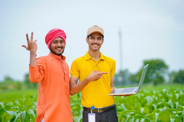 Jovem banqueiro indiano ou agrônomo mostrando alguns detalhes aos agricultores no laptop no campo de agricultura.