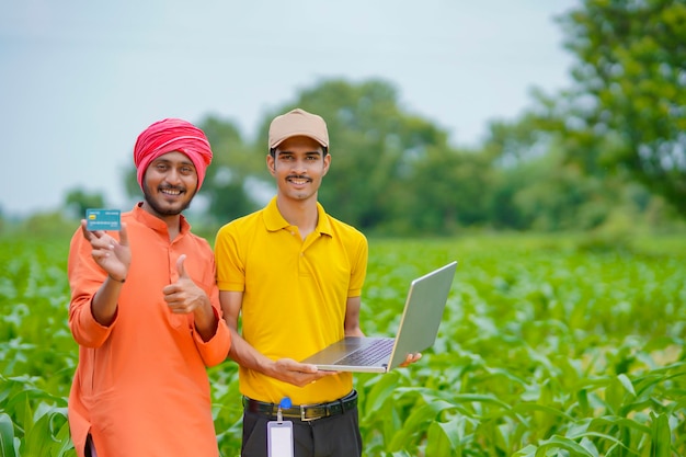 Jovem banqueiro indiano ou agrônomo mostrando alguns detalhes aos agricultores no laptop no campo de agricultura.