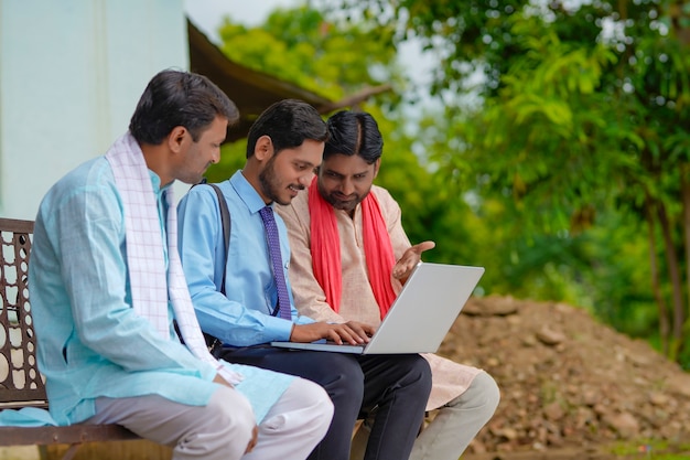 Jovem banqueiro ou agrônomo indiano mostrando alguns detalhes para fazendeiros em um laptop em casa
