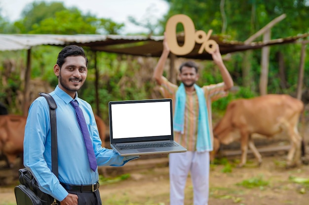 Jovem banqueiro ou agrônomo indiano mostrando tela de laptop com fazendeiro em sua fazenda
