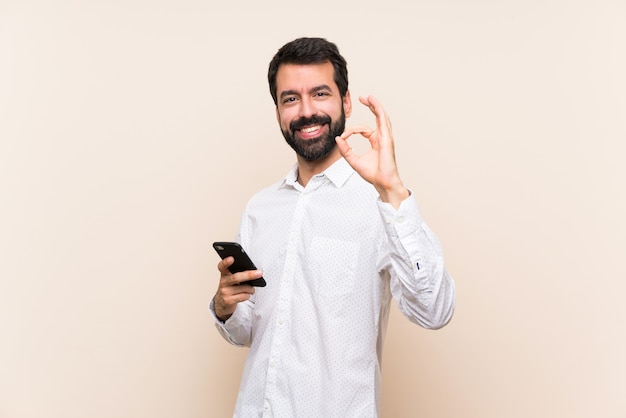 Jovem, barba, segurando, móvel, mostrando, ok, sinal, dedos