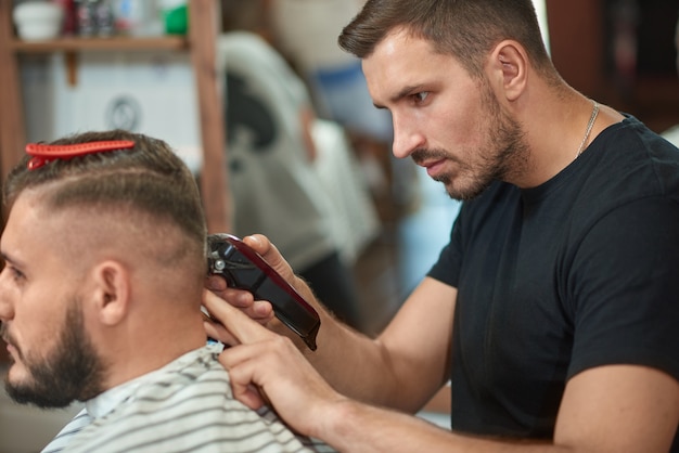 Jovem barbeiro barbudo cortando o cabelo de seu cliente