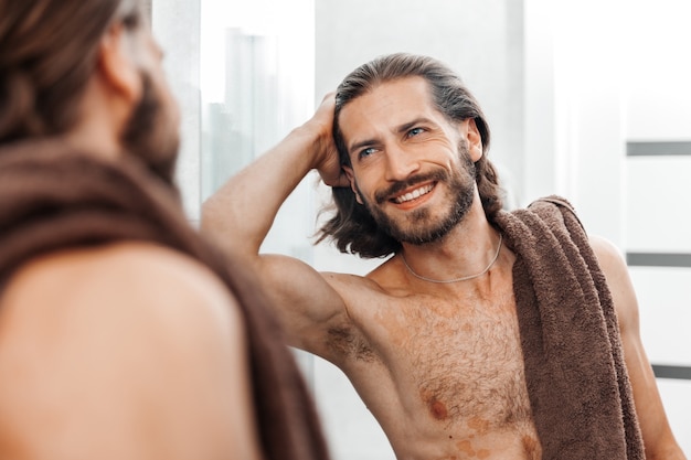 Jovem barbudo bonito olhando no espelho após o banho