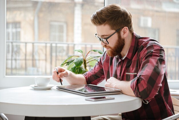 Jovem barbudo bonito usando computador tablet.