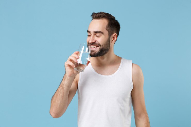 Foto jovem barbudo de 20 anos de idade pele perfeita em camisa branca segura água isolada no fundo da parede pastel azul, retrato de estúdio. conceito de procedimentos cosméticos de saúde de cuidados com a pele. simule o espaço da cópia.