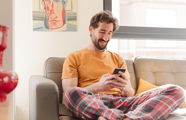 Jovem barbudo em um sofá com um telefone inteligente