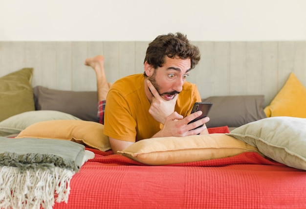 Jovem barbudo em uma cama com seu telefone celular