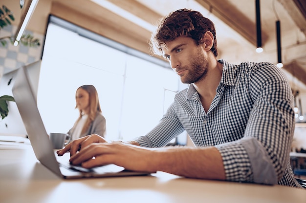 Jovem barbudo empresário de sucesso trabalhando em um laptop no escritório com uma colega