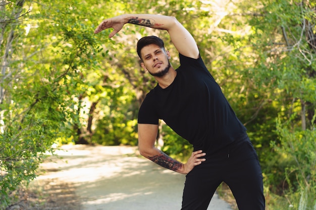 Jovem barbudo exercitando no parque antes de correr. Copie o espaço