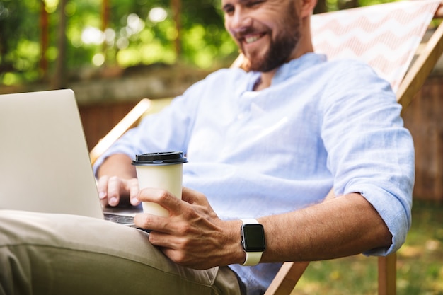 Jovem barbudo feliz ao ar livre usando um laptop