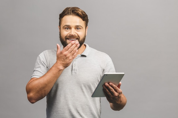 Jovem barbudo feliz em pé casual e usando tablet