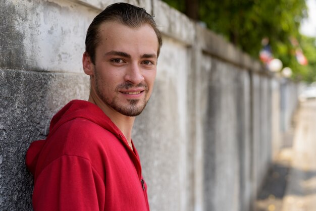 Foto jovem barbudo feliz sorrindo enquanto usava capuz vermelho nas ruas ao ar livre