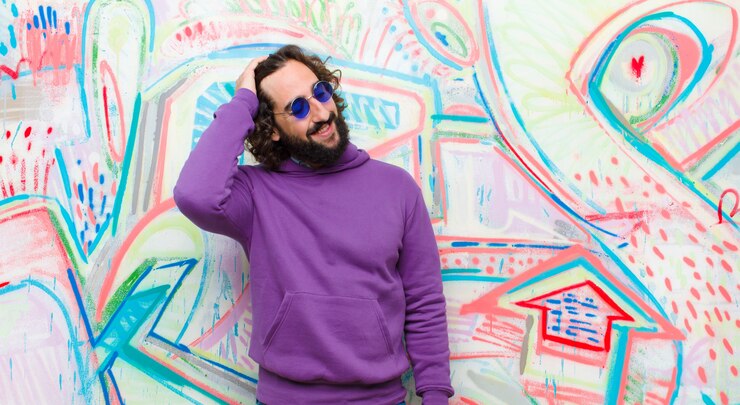 Foto jovem barbudo homem louco sorrindo alegremente e casualmente, levando a mão à cabeça com um olhar positivo, feliz e confiante na parede de graffiti