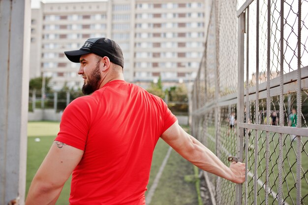 Jovem barbudo homem musculoso usar camisa vermelha, shorts e boné no estádio