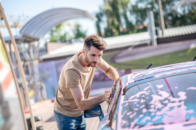 Jovem barbudo limpando vidro de carro