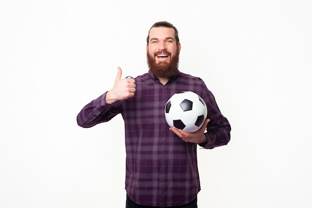 jovem barbudo mostrando o polegar e segurando uma bola de futebol