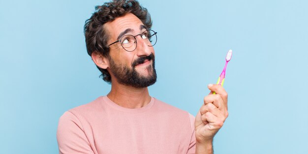 Jovem barbudo sentindo-se feliz, orgulhoso e esperançoso, imaginando ou pensando, olhando para cima para copiar o espaço com os braços cruzados