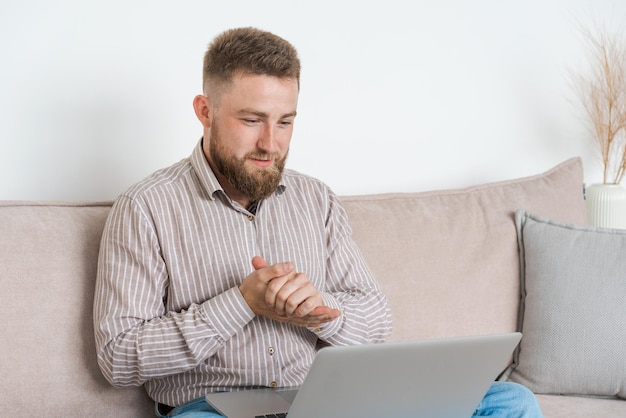 Jovem barbudo sorri enquanto lê a tela do laptop enquanto relaxa