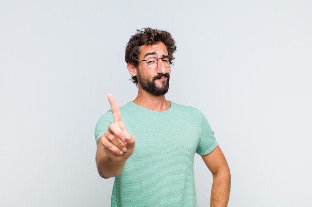 Jovem barbudo sorrindo com orgulho e confiança fazendo a pose número um triunfantemente, sentindo-se um líder