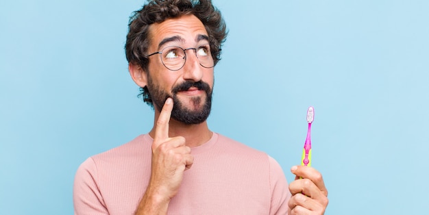 Jovem barbudo sorrindo feliz e sonhando acordado ou duvidando, olhando para o lado