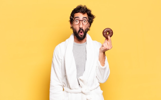 Jovem barbudo vestindo roupão e um donut de chocolate