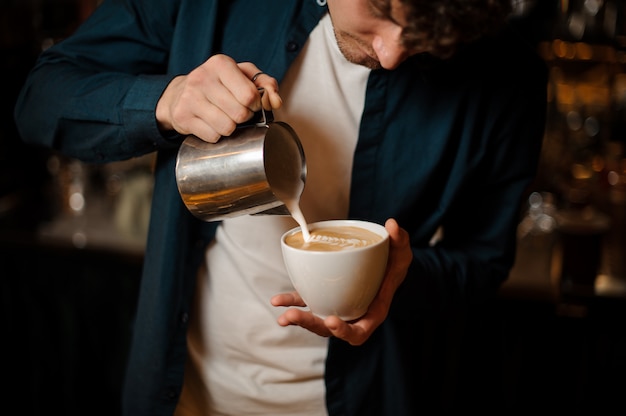 Jovem barista derramando um pouco de leite em uma xícara de café