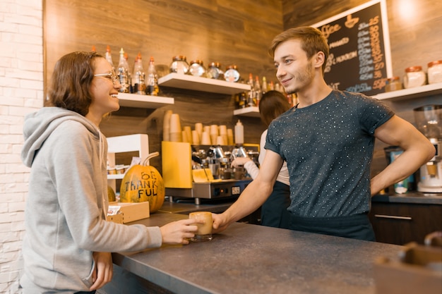 Jovem barista masculino sorridente vendendo bebida para uma garota adolescente na cafeteria