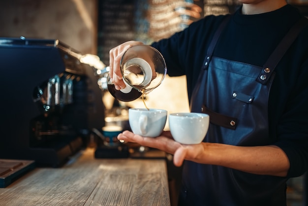 Jovem barista segurando duas xícaras de café fresco