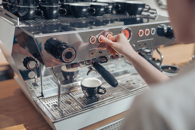 Jovem barista usando uma cafeteira moderna em uma cafeteria