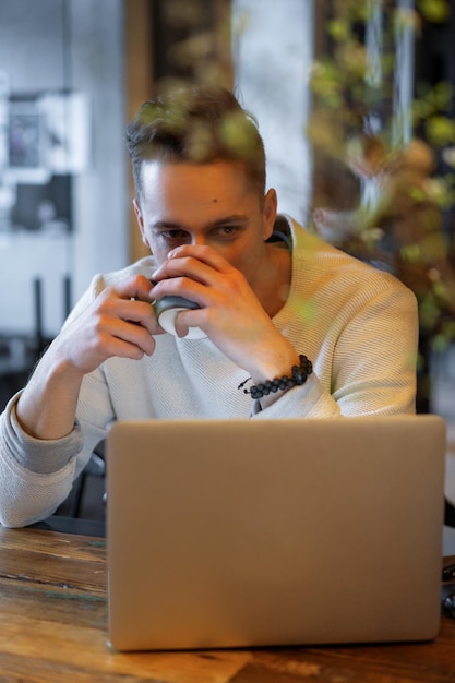 jovem bebe chá e trabalha em um laptop, freelancer trabalhando em um café