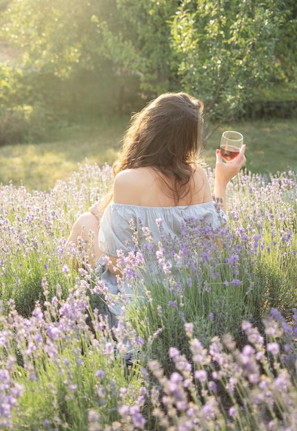 Jovem bebe vinho no campo de lavanda do sol