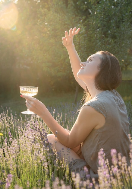 Jovem bebe vinho no campo de lavanda do sol