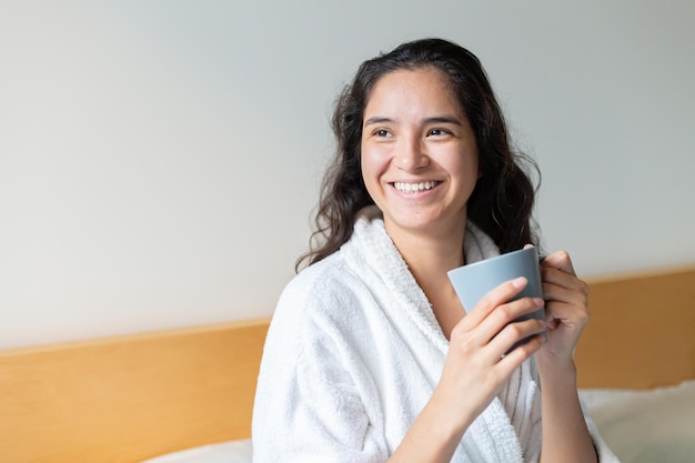 Jovem bebendo café na cama em roupão de banho