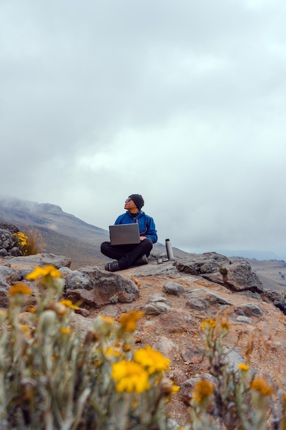 Jovem bebendo café nas montanhas com o laptop. Conceito de acampamento de montanha.