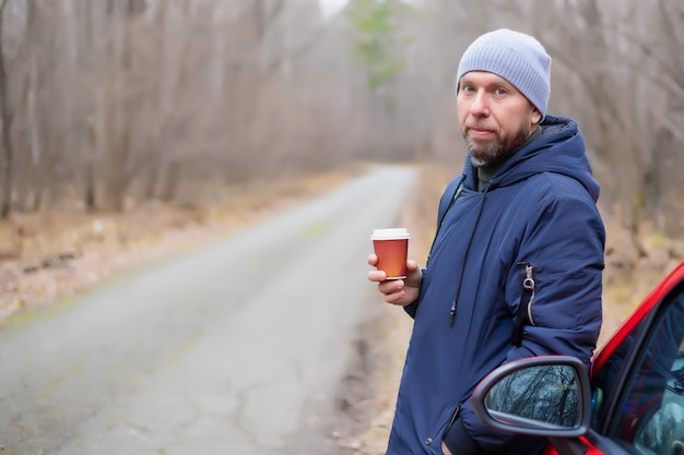 Jovem bebendo seu café perto de um carro