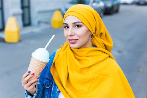 Jovem bela mulher árabe em hijab bebendo um coquetel de refrigeração ao ar livre.