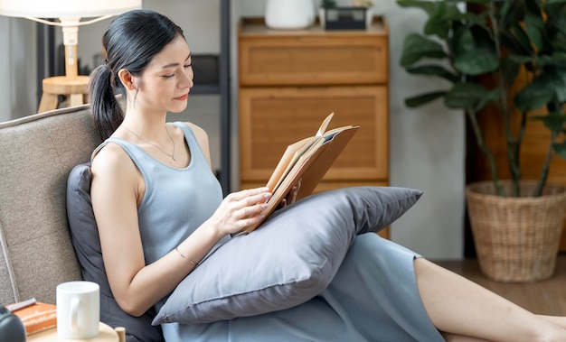 Jovem bela mulher caucasiana relaxando enquanto lê um livro no sofá em casa