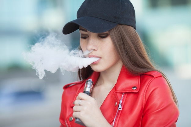 Jovem bela mulher fumando (vaping) e-cigarro com fumaça